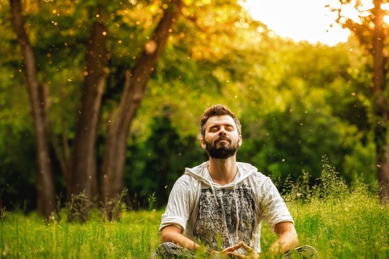 678758-1789570801 A man sitting on grass in the park and smiling with eyes closed by maxpetrov @ادوبي ستوك