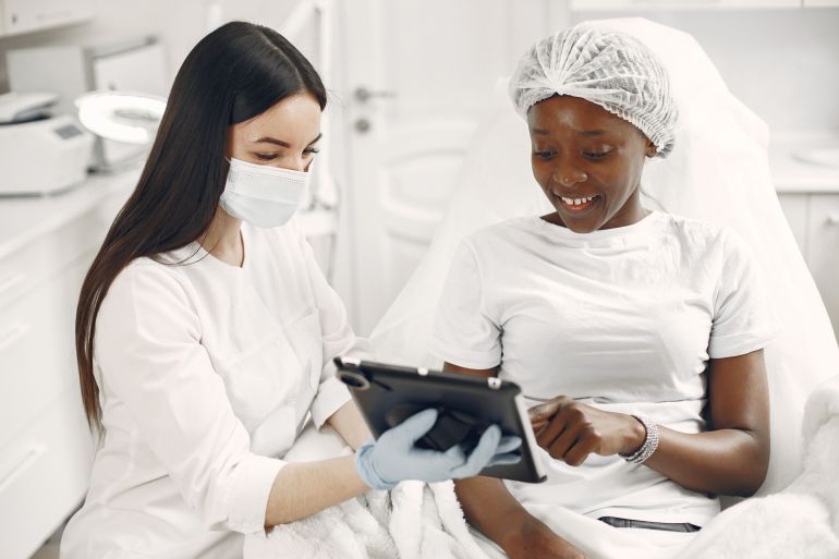 7446684-1788619709 Smiling patient and dermatologist using tablet during skincare consultation.