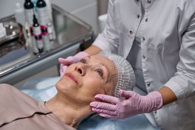 7582555-1788617862 A mature woman in a spa receiving a relaxing facial treatment from a professional in a medical clinic setting.