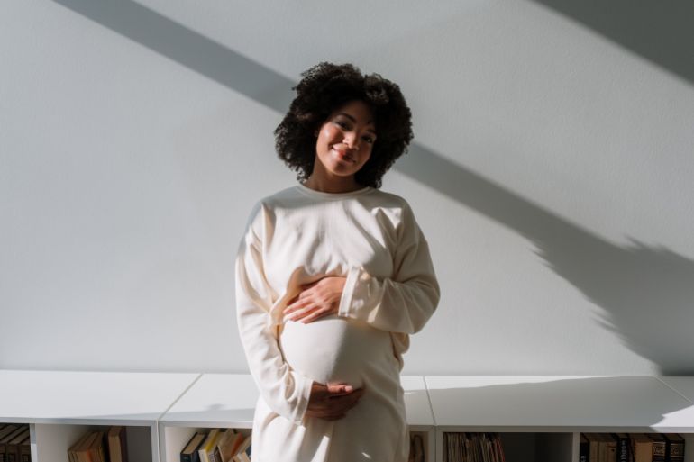 853662-1790261321 Beautiful pregnant woman with curly hair embracing maternity in a serene indoor setting.