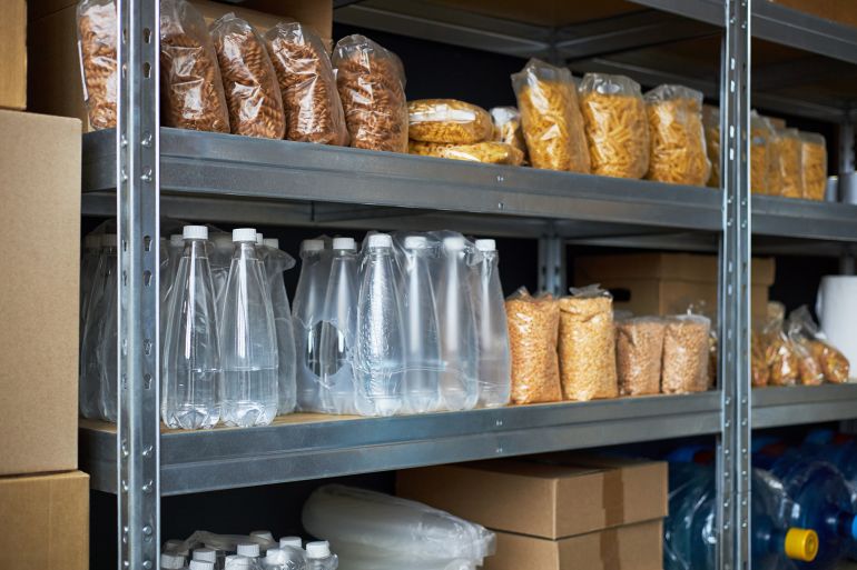 Shelves filled with packaged food and bottled water in a storage area. Supplies neatly organized on metal racks with various items including pasta and ... See More by DragonImages @ادوبي ستوك