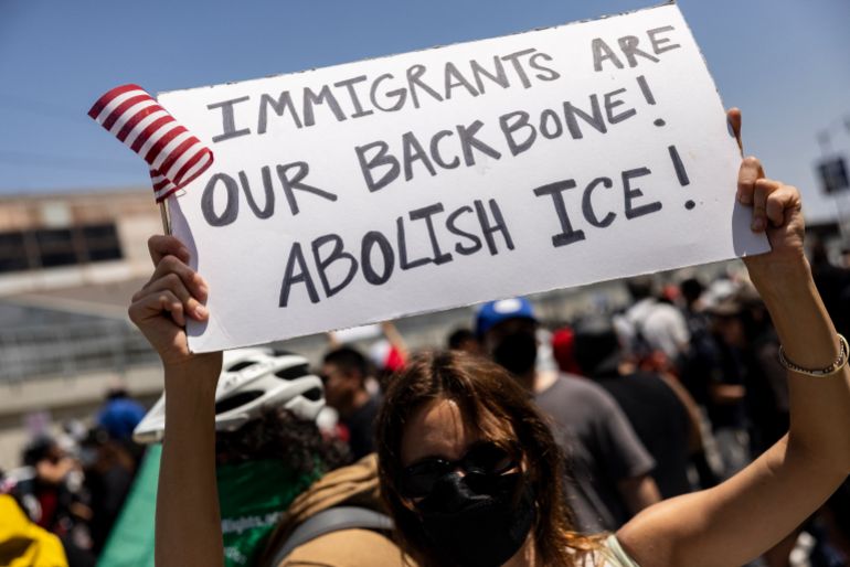 afp_6846c5d51d47-1749468629 A demonstrator holds a poster reading “Immigrants are our backbone! Abolish Ice!” in front of National guards during clashes with law enforcement in front of the federal building during a protest following federal immigration operations, in Los Angeles, California on June 8, 2025.
