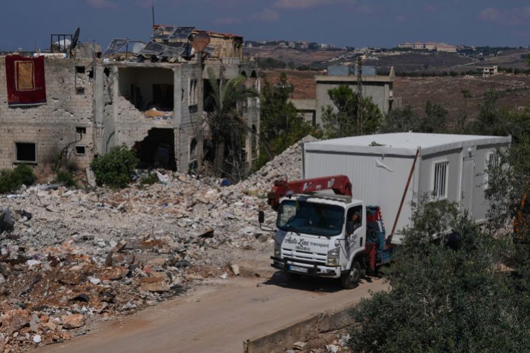 ap_6ab11a9e2b272-1789991582 A truck carrying a prefabricated unit passes among destroyed houses in Zawtar al-Gharbieh, southern Lebanon, Monday, Sept. 21, 2026, as they arrive to provide housing for families whose homes have been destroyed in the fighting between Hezbollah and Israel. (AP Photo/Mohammed Zaatari)