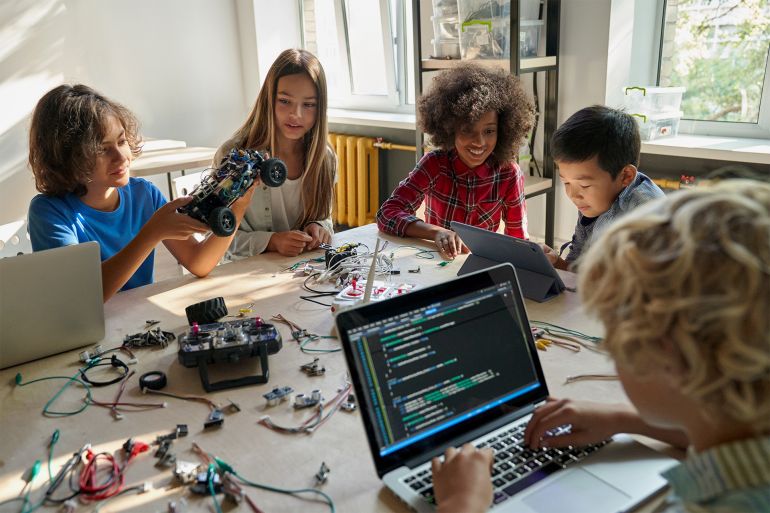 gettyimages-1338344348-1691164906 Diverse school children students build robotic cars using computers and coding. Happy multiethnic kids learning programming robot vehicles sitting at table at STEM education science engineering class.