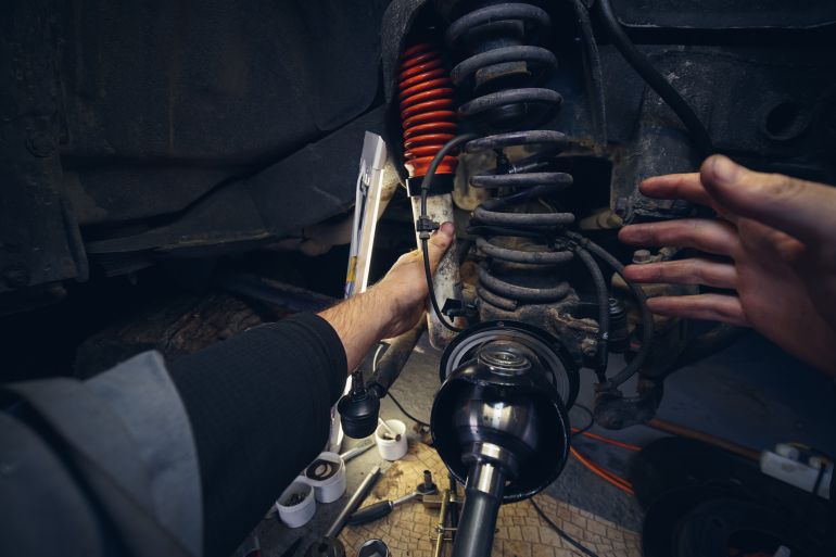gettyimages-1443971579-1789911833 Car service from the first person mechanic. Male hands. Repair of the front wheel hub, replacement of Springs and shock absorber. four-wheel drive SUV.
