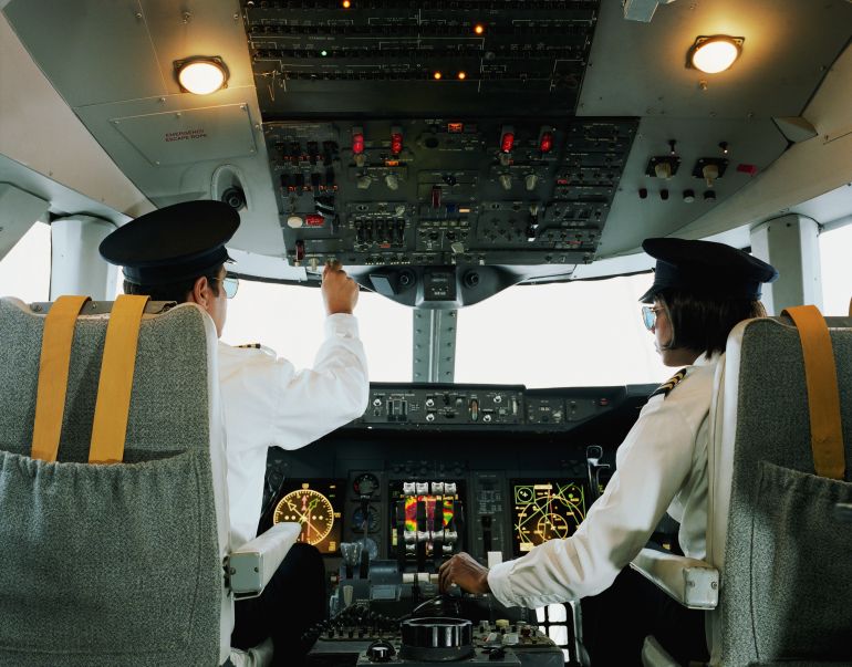 Male and female aeroplane pilot, operating controls, rear view - stock photo