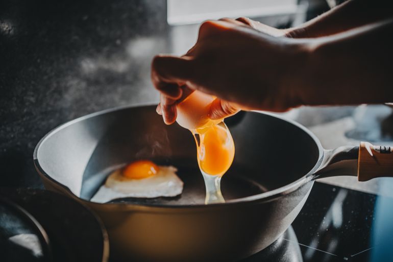 Close-up of female hand cracking an egg into a sizzling hot frying pan as she prepares a healthy breakfast in kitchen in the morning. Clean eating and healthy eating habits with natural ingredients. Wellness lifestyle and mindful meal preparation
