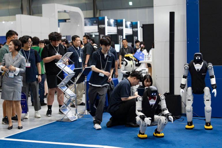 Visitors watch and photograph Agibot humanoid robots performing a dance routine at the AI Summit Seoul & Expo 2026 held at COEX in Seoul, South Korea, on August 19, 2026. The three-day exhibition features artificial intelligence infrastructure, enterprise data storage solutions, GPU-accelerated computing systems, and generative AI software workflows from global tech companies including Seagate, HP Korea, NVIDIA, and Adobe. (Photo by Chris Jung/NurPhoto via Getty Images)