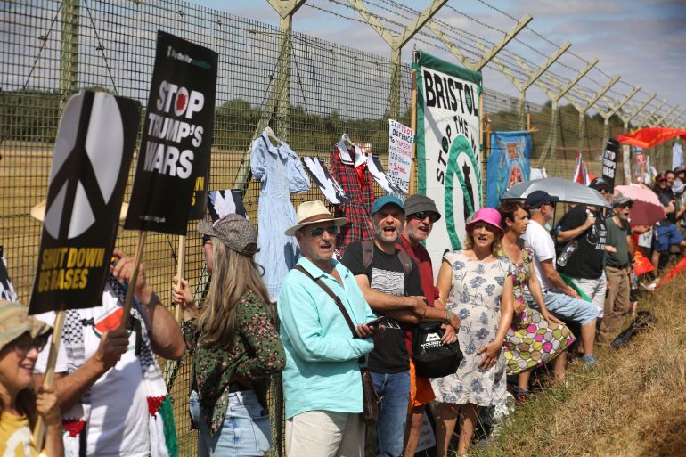 gettyimages-2290605622-1786971130 FAIRFORD, ENGLAND - AUGUST 15: Protesters stand against the fence with signs and flags during the demonstration on August 15, 2026 in Fairford, England. Various anti-war groups including supporters of CND and Stop The War UK gather to call on Andy Burnham to end Donald Trump's use of British bases to bomb and attack Iran. (Photo by Martin Pope/Getty Images)