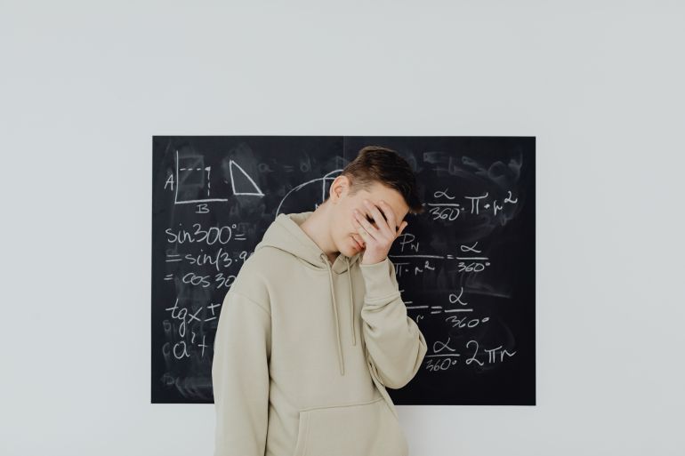 picsw3-4-1788441141 Teen boy covers face in frustration in front of a chalkboard filled with math equations, reflecting academic stress. المصدر:magnific