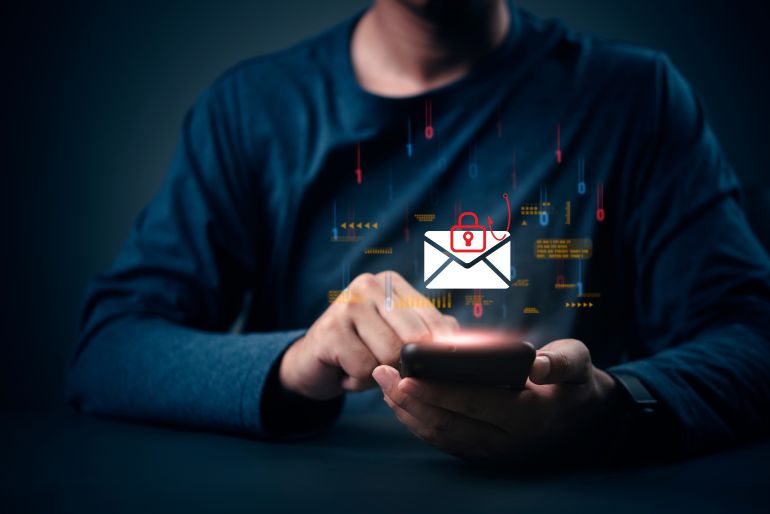 shutterstock_2700045939-1779704160 Cybersecurity threat, phishing email scam concept. Man hand on phone, data breach danger. Hacker attack, internet fraud, password stealing. Spam message, virus, security risk warning.