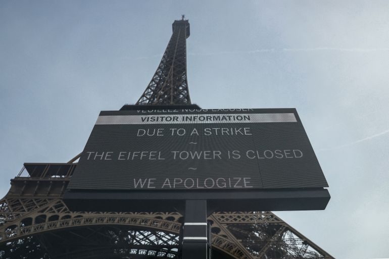 (FILES) This photograph shows a view of a placard reading "Due to a strike the Eiffel Tower is closed, we apologize" with the Eiffel Tower in the background, amid a nation-wide day of strike called by France's eight biggest workers unions for "social justice" measures, in Paris, on October 2, 2025. The Eiffel Tower is set to reopen on September 8, 2026, after a day of strike action by staff outraged by the eviction of female staff during a visit granted to a Hindu religious group, which apologized but denied having refused access "to anyone". (Photo by Alain JOCARD / AFP)