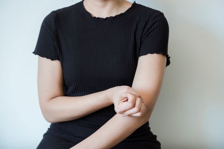 017032-1792809059 A close-up view of a woman in a black shirt holding her arm, showcasing skin contact and emotion.