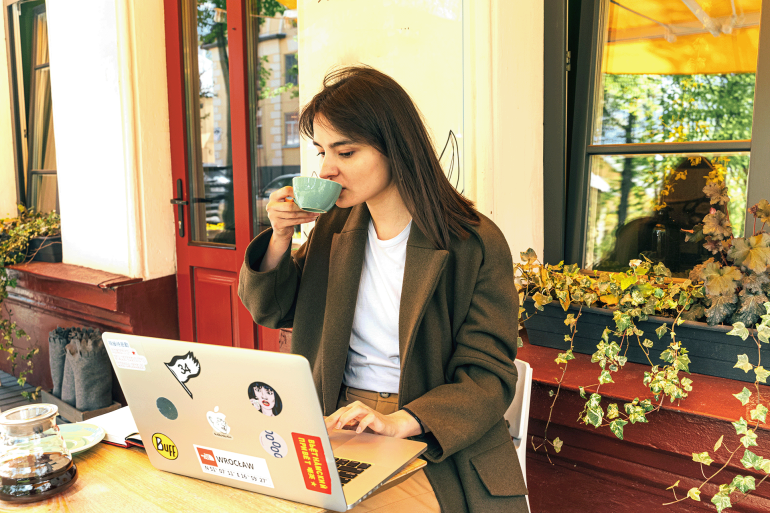 02-1791915968 Young woman drinking coffee and working on laptop in outdoor cafe setting.