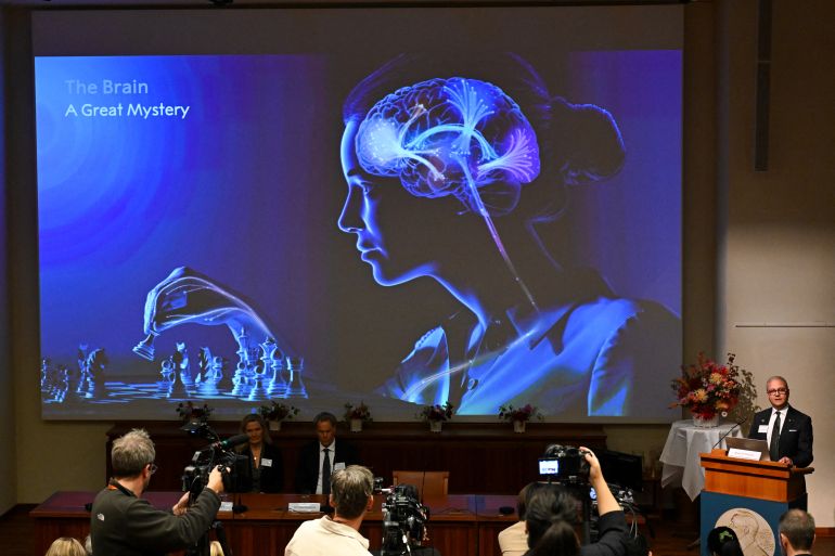 3nobel-prize-1791194280 Karolinska Institute neuroscience professor Abdel El Manira speaks in front of a screen displaying an illustration of the human brain during the announcement of the winners of the 2026 Nobel Prize in Physiology or Medicine at the Karolinska Institute in Stockholm, Sweden, on October 5, 2026. US scientist Karl Deisseroth and German scientists Peter Hegemann and Georg Nagel share the 2026 Nobel Prize in Physiology or Medicine for their discoveries concerning light-gated ion channels and optogenetics. (Photo by Jonathan Nackstrand / AFP)