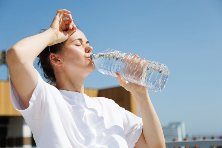 4heat-stress-1785839884 Woman drinking water during an extreme summer heatwave outdoors. Hydration, hot weather, high temperatures, heat safety, sun exposure and prevention of dehydration. adobe stock