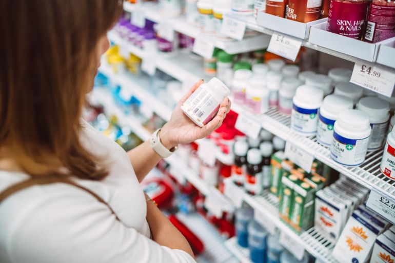 Woman carefully reads the label of a supplement bottle while shopping in the pharmacy section. Concept of healthy lifestyle, nutrition, self-care, and wellness.