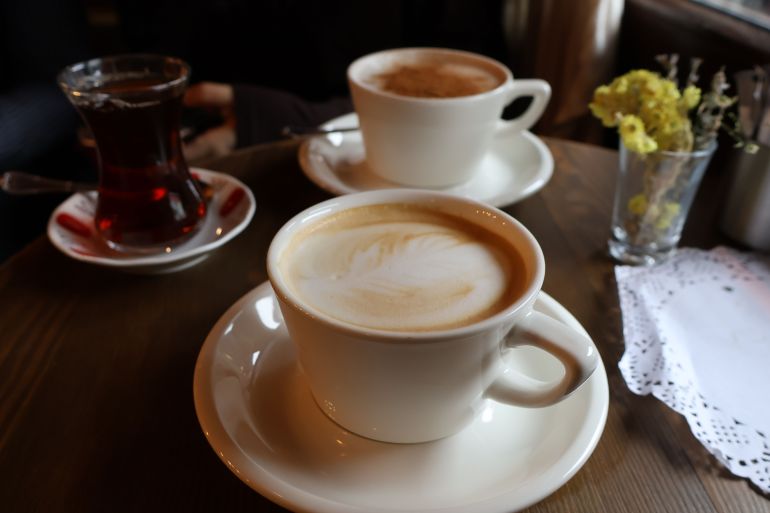 5967477-1791546570 Inviting scene with two lattes and a tea glass on a wooden table, perfect for coffee shop vibes.