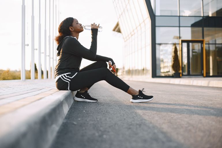 69395-1790697046 An African American woman takes a break during her workout to hydrate with a water bottle.