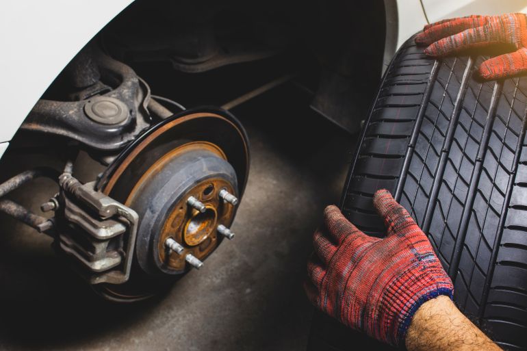6car-1791629033 The mechanic's hand holding black tires for changing alloy wheel into the wheel hub at car tire shop. adobe stock
