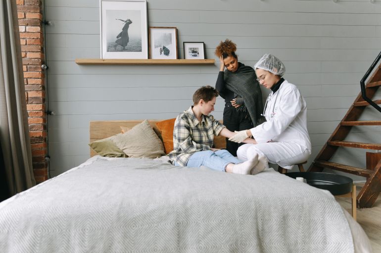 7659694-1792809885 A doctor offers supportive care to a patient in a cozy bedroom setting, fostering recovery.