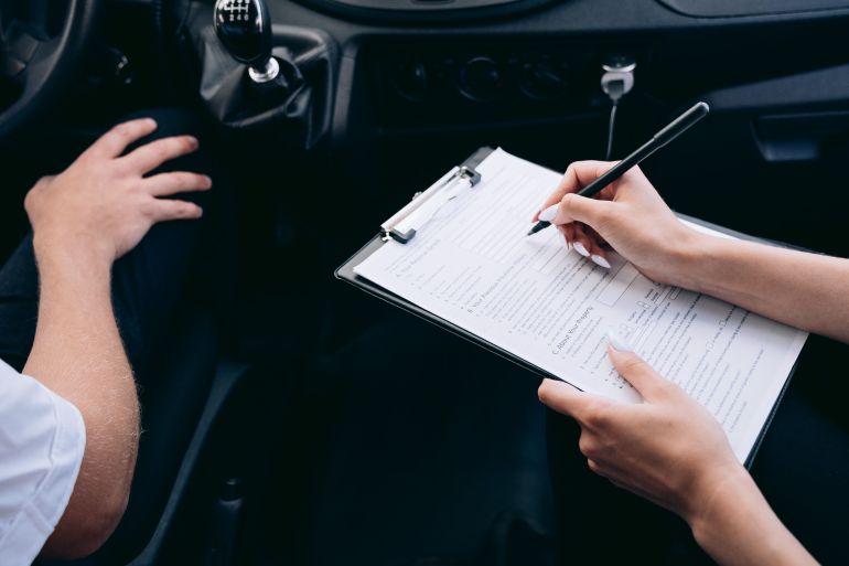 8943323-1792762183 Close-up of a person writing on a clipboard inside a car, showing hands and a gear shift.