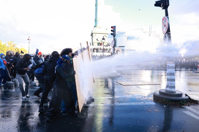 Protesters face a water cannon during a demonstration of high-school students at Place de la Bastille, in Paris, on October 8, 2026, as part of a nationwide protest movement over learning conditions. Since late September, pupils have barred the entrances to hundreds of schools, complaining of teacher absences, overloaded timetables, dilapidated classrooms and buildings ill-adapted to rising temperatures, among other grievances. (Photo by Kenzo TRIBOUILLARD / AFP)