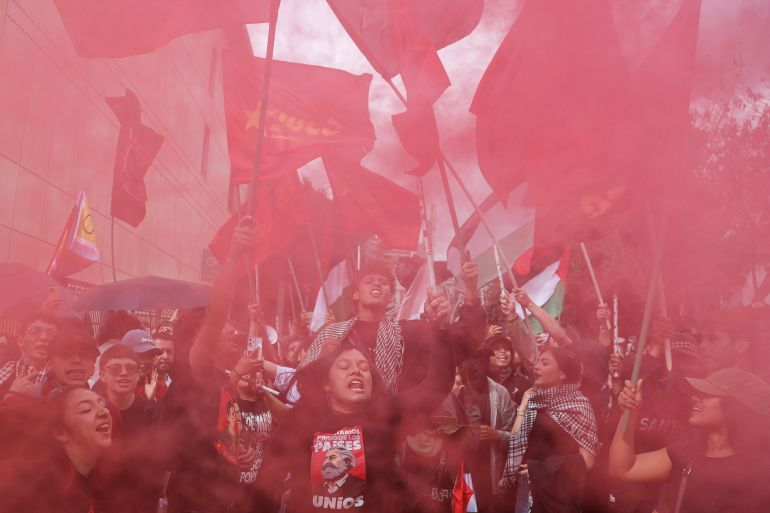 afp_6ad0a466b07d-1792058470 TOPSHOT - Demonstrators are enveloped in red smoke from flares during a protest against the government of Colombian President Abelardo de la Espriella in Bogota on October 14, 2026, as part of a nationwide day of demonstrations called by labor unions, teachers' organizations, student groups and opposition sectors. (Photo by Andrea ARIZA / AFP)
