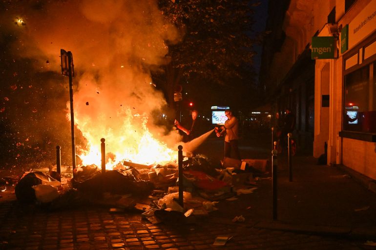 afp_6ad5195856cc-1792350552 TOPSHOT - Inhabitants use a fire extinguisher on burning trashes near Oberkampf metro station at Place de la Republique following an unauthorised demonstration, central Paris, on October 18, 2026 a day after nationwide protests against the "high cost of living".