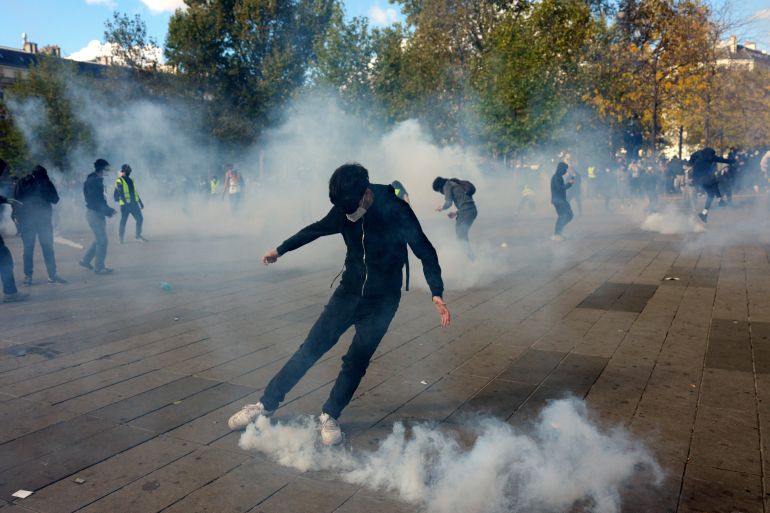 getty_6ad37fc33f-1792245699 PARIS, FRANCE - OCTOBER 17: A protester kicks a smoke grenade at the Place de la République during the latest student protests on October 17, 2026 in Paris, France. The involvement of the Gilets Jaunes (Yellow Vests) with the ongoing French school blockades expands the scope of these demonstrations by linking localised student grievances to broader economic policies. Student unions originally initiated the movement to protest underfunding, deteriorating infrastructure, and acute teacher shortages across French high schools and universities. By joining the protests, the Gilets Jaunes introduce their established platform against austerity cuts, rising living costs, and surging fuel prices into the youth-led action. (Photo by Carl Court/Getty Images)