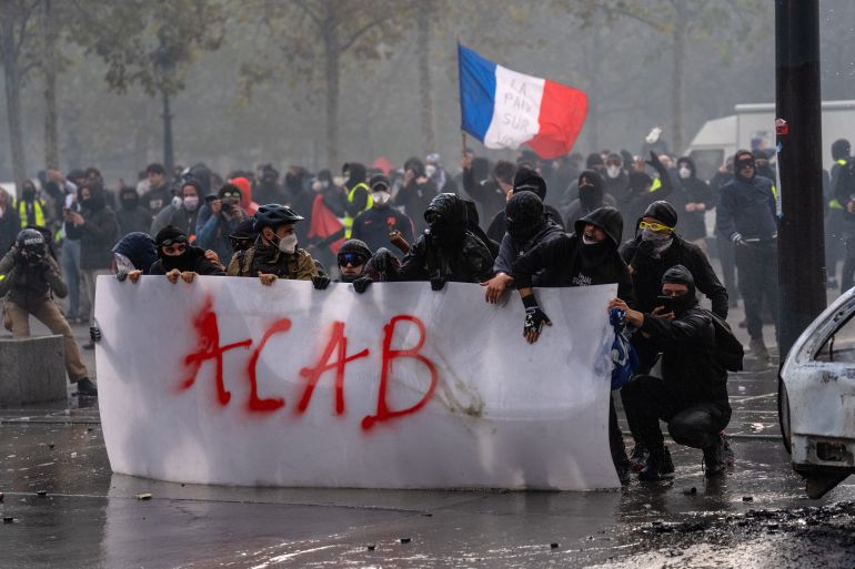 getty_6ad5fd5f84-1792408927-1 PARIS, FRANCE - OCTOBER 17: Protesters shield themselves behind a plastic banner as police fire a water cannon during demonstrations on October 17, 2026 in Paris, France. The involvement of the Gilets Jaunes (Yellow Vests) with the ongoing French school blockades expands the scope of these demonstrations by linking localised student grievances to broader economic policies. Student unions originally initiated the movement to protest underfunding, deteriorating infrastructure, and acute teacher shortages across French high schools and universities. By joining the protests, the Gilets Jaunes introduce their established platform against austerity cuts, rising living costs, and surging fuel prices into the youth-led action. (Photo by Carl Court/Getty Images)