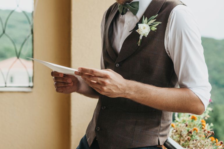 Close-up of a groom holding a sheet of paper in his hands with an oath or invitation. Preparing for the wedding.
