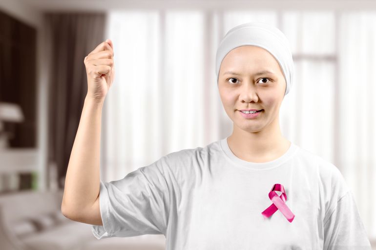 gettyimages-1181124968-1759687574-1 Asian woman in a white shirt with a pink ribbon on the home. Breast cancer awareness
