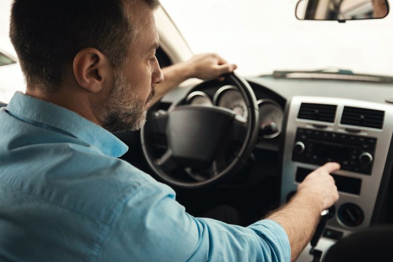 gettyimages-1477841653-1791309956 Road Playlist. Rear Back Over Shoulder View Of Man Driving Car And Listening To Music On Auto Audio System, Checking Automobile Options During Test Drive Pushing Button On Dashboard Turning On Radio