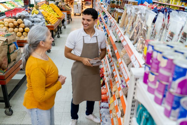 gettyimages-1497211539-1793046668 Latin American senior woman asking a question to salesman at the supermarket while looking at the products on shelf - Lifestyles concepts