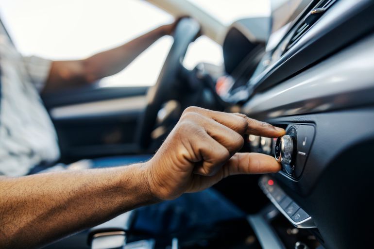 gettyimages-2192535188-1791309936 Close up of multicultural car driver's hand turning up volume on radio in an auto.