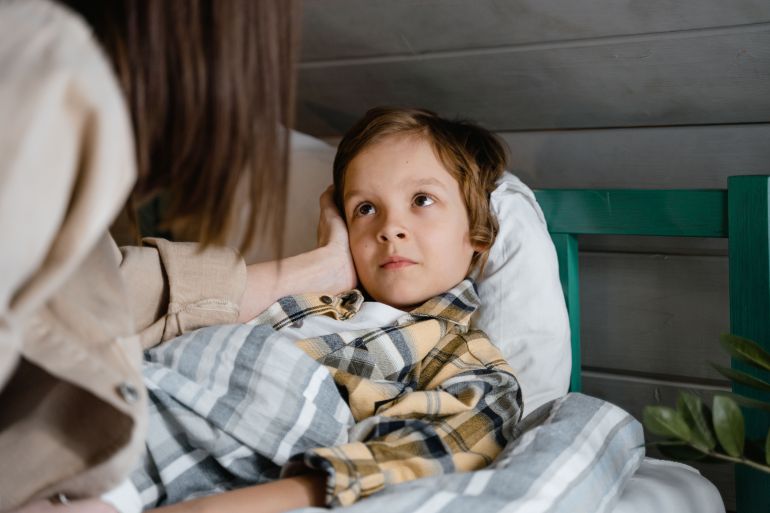 n-7641358-1791636202 A parent gently comforts a child lying in bed. Warm and tender moment captured indoors.