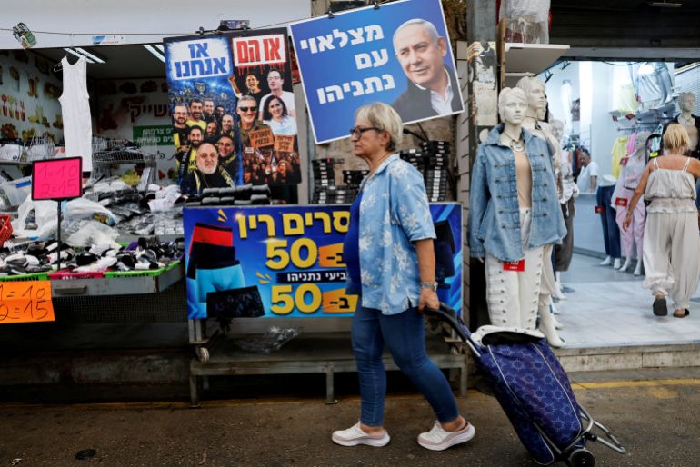 reuters_6ad13349-1792095049 A woman walks past a sign featuring an image of Israeli Prime Minister Benjamin Netanyahu at a market, ahead of Israel's national election, in Ramla, Israel, October 14, 2026. REUTERS/Amir Cohen