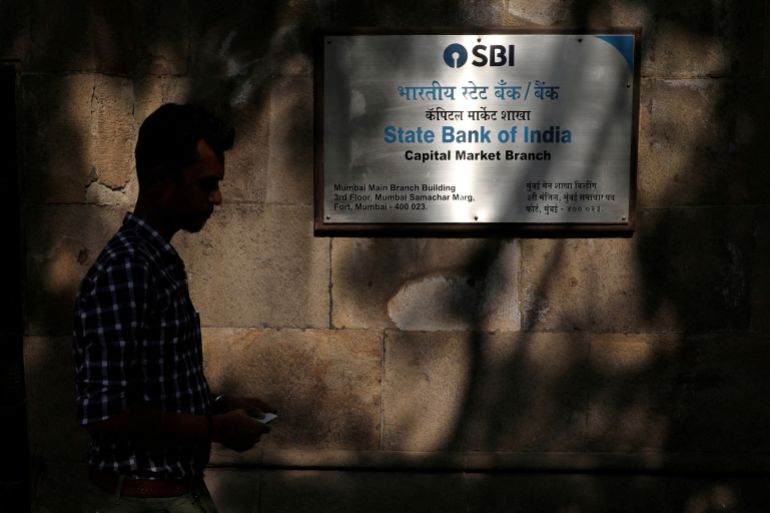 reuters_6ad9d88f-1792661647 FILE PHOTO: A man walks in front of a signboard displayed at the head office of State Bank of India (SBI) in Mumbai, India, April 18, 2023. REUTERS/Niharika Kulkarni/File Photo