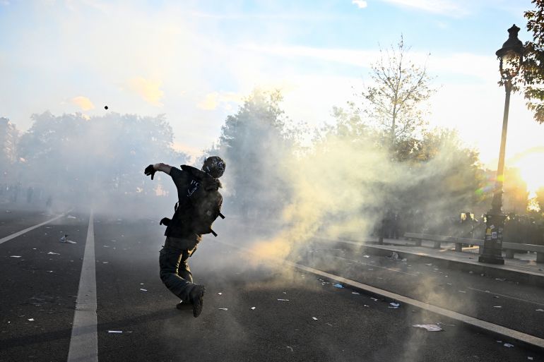 A protester throws a tear gas canister back at police during a demonstration of high-school students at Place de la Bastille, in Paris, on October 8, 2026, as part of a nationwide protest movement over learning conditions. Since late September, pupils have barred the entrances to hundreds of schools, complaining of teacher absences, overloaded timetables, dilapidated classrooms and buildings ill-adapted to rising temperatures, among other grievances. (Photo by JULIEN DE ROSA / AFP)