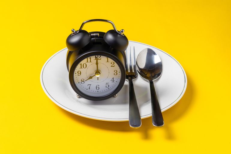 shutterstock_2729032267-1773163457 Empty plate with clock on a yellow background, intermittent fasting concept; Shutterstock ID 2729032267; purchase_order: aj; job: ; client: ; other: